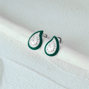 Macro detail of green enamel teardrop earrings with crystals on a textured branch