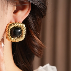 Detail eines vintage goldfarbenen quadratischen Ohrrings mit schwarzem Edelstein am Ohr