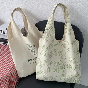 Detail of minimalist cream canvas tote bag with green leaf pattern on a black chair