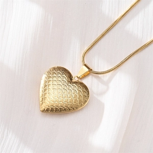 Detailed close-up of a gold heart-shaped locket necklace with vintage embossed patterns