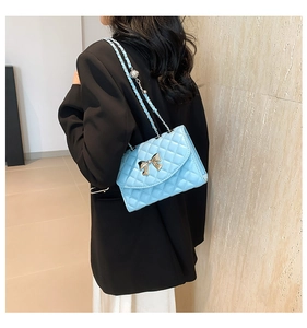 Quilted light blue crossbody bag with bow hardware shown on model in black suit