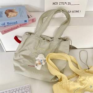 Detail of embroidered lamb motif on drawstring canvas tote bags in sage green and yellow