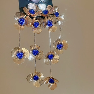 Detailed close-up of long tassel earrings with golden hollow flowers and blue beads