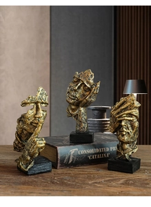 Detailed view of three gold abstract face sculptures on black bases on a wooden desk
