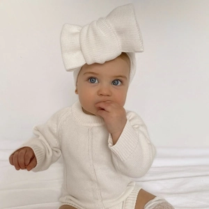 Close-up of a baby wearing a white knitted bow headband made of soft elastic fabric