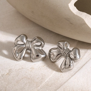Close-up of polished silver bow-shaped earrings on a textured stone background