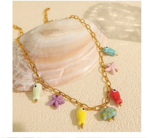 Close-up of gold chain necklace with colorful enamel fish and starfish charms on a shell