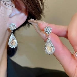 Close-up of floral stud and teardrop crystal earrings in polished silver finish