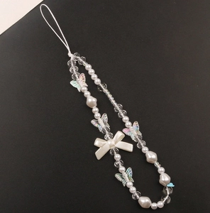 Detail of beaded phone charm with iridescent butterflies and white bow on black background