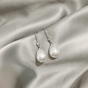 Detailed view of teardrop pearl earrings with silver rhinestone hooks on silk fabric