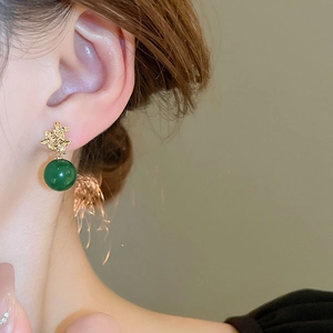 Detail eines Vintage-Gold-Ohrrings mit dunkelgrüner Harzperle am Ohr getragen