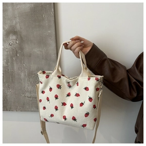 Detail of beige corduroy tote bag featuring red strawberry patterns and canvas handle