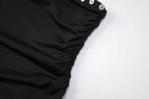 Détail du tissu noir avec design froncé latéral et trois boutons nacrés blancs sur le côté
