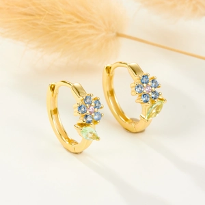 Macro view of gold hoop earrings with colorful zircon flowers and green leaves