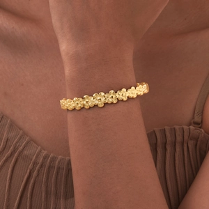 Close-up of gold stainless steel hollow heart flower bangle on woman's wrist