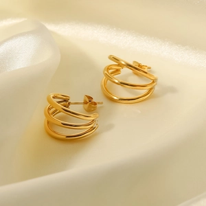 Macro view of gold-plated geometric multi-hoop earrings on soft cream silk fabric