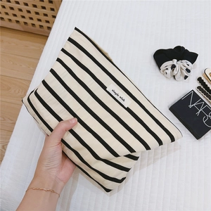 Detail of striped cotton makeup bag held by hand, featuring the Simple Wish woven label
