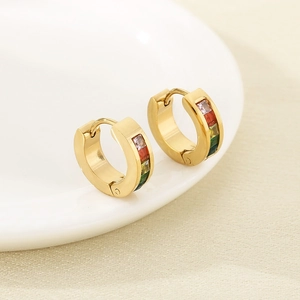Détail de boucles d'oreilles rondes dorées serties de zircons colorés sur plateau blanc