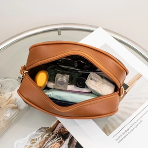 Brown faux leather oval vanity bag with gold zipper showing internal storage space
