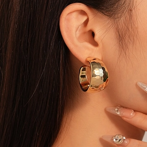 Close-up of a wide C-shaped gold earring with irregular hammered metal texture on model