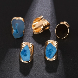 Detail view of five blue druzy agate gold plated rings on a textured black background