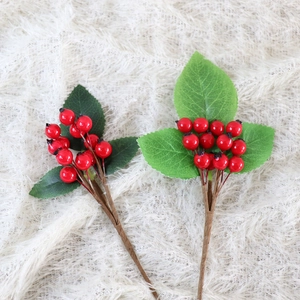 Lifelike red artificial berry branches with green leaves on white plush background
