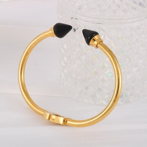 Detailed close-up of gold stainless steel bangle with black cone studs on silk fabric