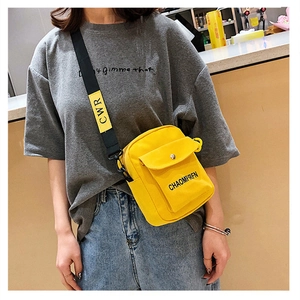 Detail of yellow canvas crossbody bag featuring a wide black strap with CWR lettering