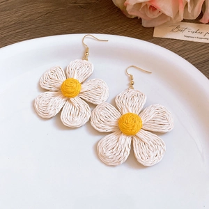 Handmade raffia flower earrings with yellow centers and gold hooks on a ceramic tray