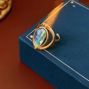 Macro detail of adjustable gold ring featuring an oval abalone shell inlay on a jewelry box