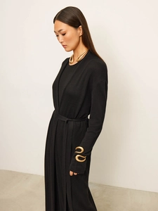 Detail of a black knit long sleeve dress with gold sculptural accessories and tie waist