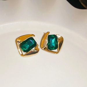 Dettaglio di orecchini vintage dorati con gemme verde smeraldo su vassoio bianco