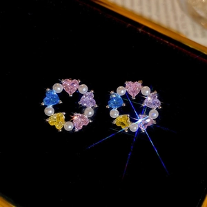 Macro shot of silver stud earrings with colorful heart zircons and white pearls