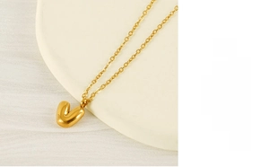 Detailed close-up of a golden bubble-style letter V pendant on a fine cross chain necklace