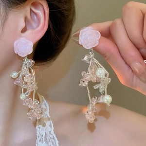 Détail de boucles d'oreilles à pompons fleuris avec roses en résine rose et perles