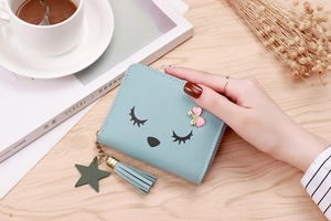 Detail of light blue wallet with cartoon eyelash design, pink bow, and tassel charm