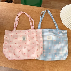 Close-up of canvas tote bag featuring cute pink bow print and classic plaid pattern texture