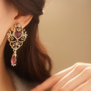 Close-up of vintage gold heart earring with purple gemstones and crystals on model