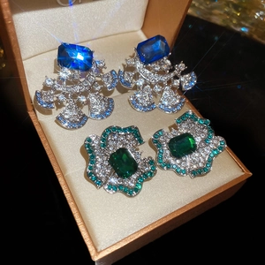 Detailed close-up of luxury flower earrings with blue and green gems in a gift box