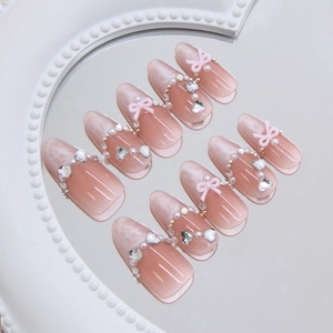 Pink cat eye press-on nails with white 3D bows, pearls, and heart rhinestones