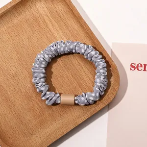 Close-up of a grey polka dot fabric scrunchie with a nude rectangular buckle on wood