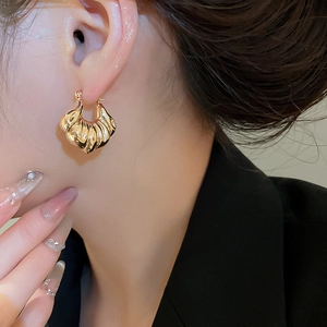 Close-up of golden shell-textured hoop earrings worn by a model in soft lighting