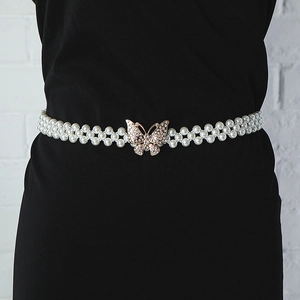 Detail of elastic pearl belt with gold butterfly buckle on a black dress