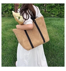 Detailed texture of the hollow woven straw tote bag with black shoulder straps for vacation
