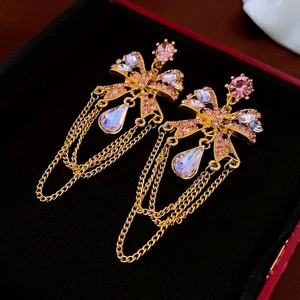 Macro detail of golden bow earrings with pink rhinestones and cascading metal tassels