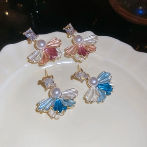 Detail view of gold-plated petal earrings with pearls and zircons on a white ceramic plate