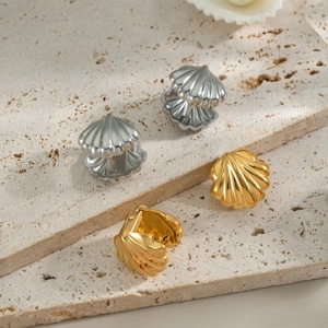 Close-up of gold and silver shell earrings with striped texture on stone surface