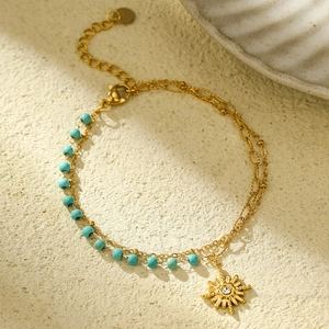 Macro view of 18K gold plated sun pendant with blue beads and heart charm bracelet