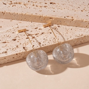 Detail of transparent cherry earrings with silver glitter on beige travertine