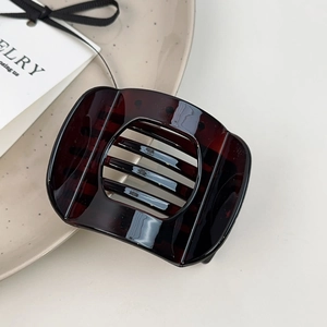 Detail of square dark tortoiseshell hair clip with cut-out design on a ceramic plate